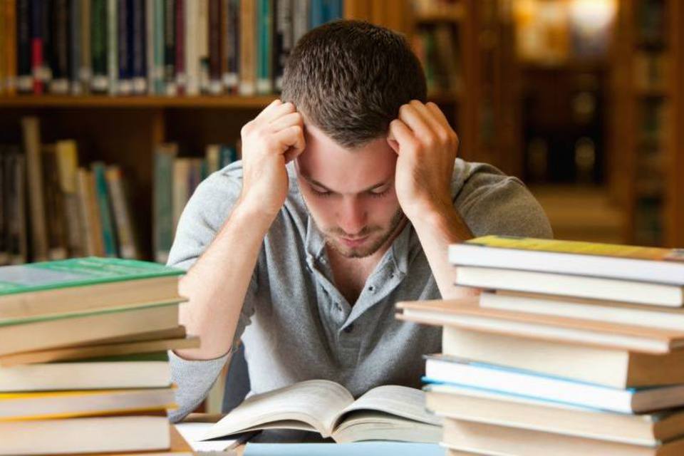 imagem de homem em mesa de estudos, de cabeça baixa pensando, com vários livros - Passar no ENCCEJA é difícil
